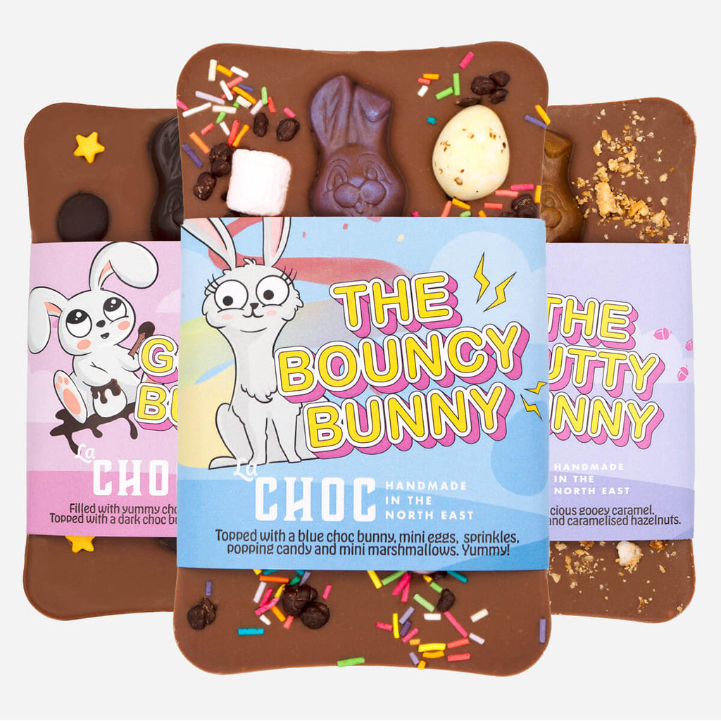 A trio of La Chocolatrice's handmade Easter chocolate bars, featuring "The Bouncy Bunny" with colourful sprinkles, mini eggs, and a blue chocolate bunny, alongside "The Nutty Bunny" and "The Gooey Bunny," each with unique toppings and playful packaging.