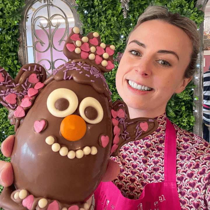 Smiling woman holding a handmade, decorated chocolate Easter egg during an Easter egg-making workshop at La Chocolatrice in the North East.